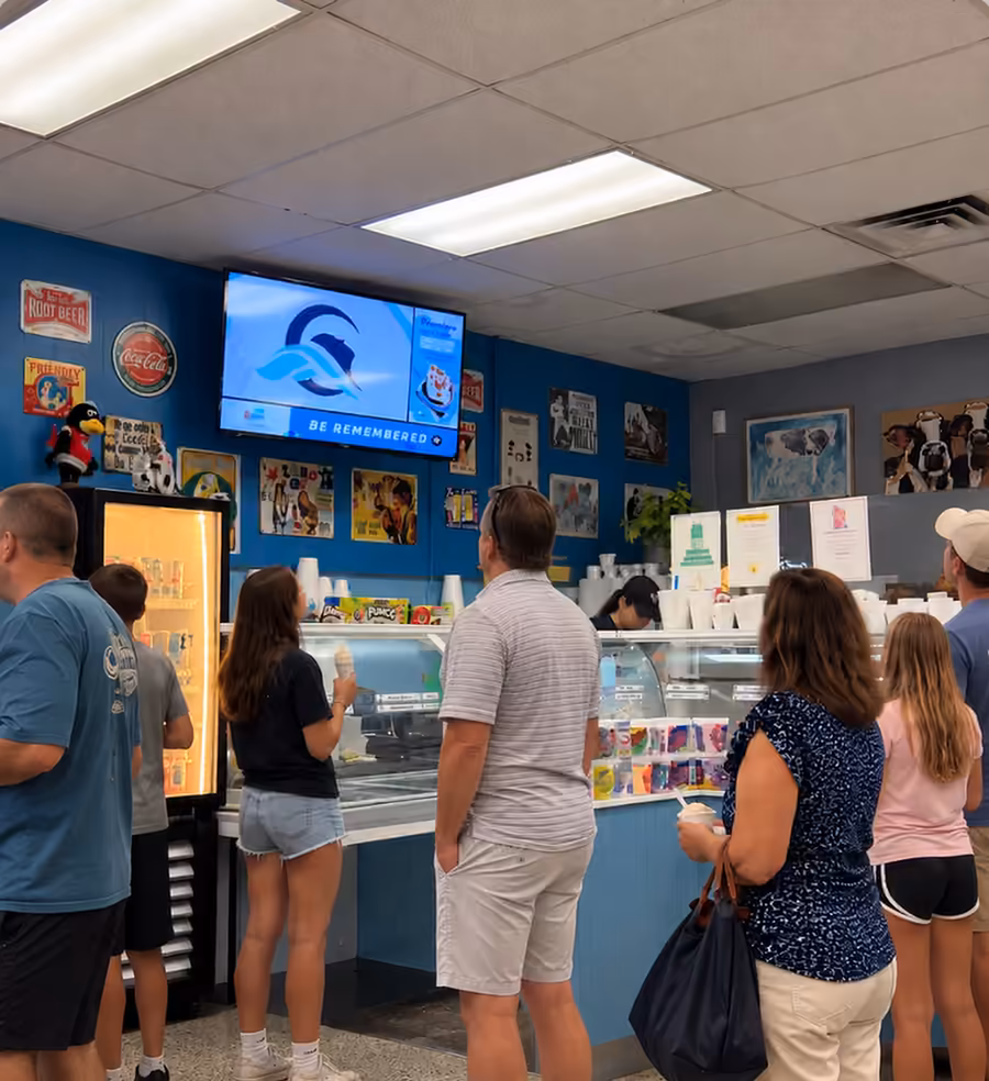 Customers at the Cold Cow ice cream counter with a digital screen on the wall